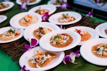 Small paper plates with food piled on a table next to orchids