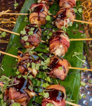 skewered bacon wrapped with dark sauce and small micro greens